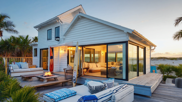Modern beachfront beach house with outdoor deck, fire pit, surfboards, and panoramic ocean views at sunset
