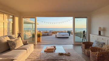 Luxury beachfront living room with panoramic ocean view, sliding glass doors, spacious deck, and outdoor hot tub at sunset